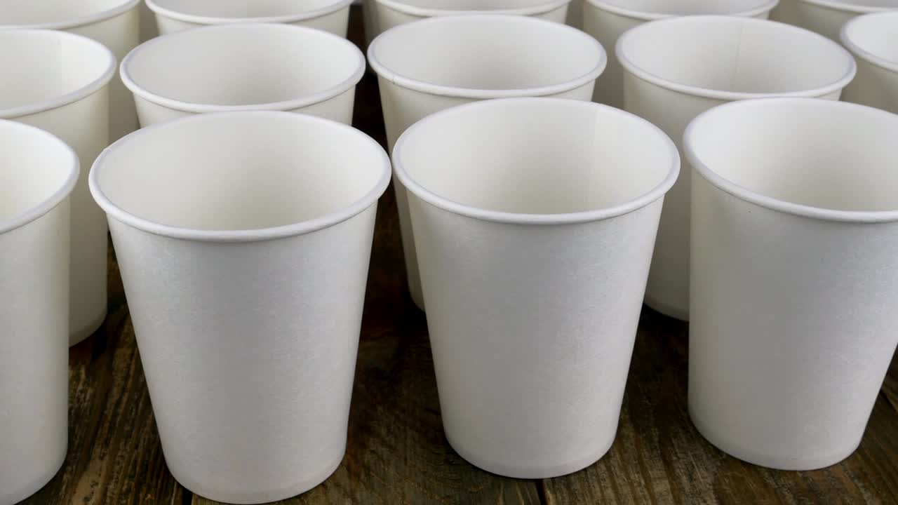 어두운 배경에서 커피 또는 뜨거운 음료를위한 색 일회용 종이 컵의 줄은 천천히 회전합니다.