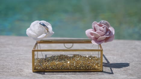 wedding bands nestled in flowers atop a glitter-filled glass box