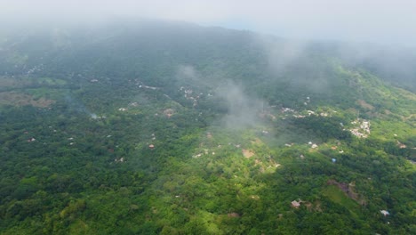 Una-Vista-Aérea-De-Colinas-Cubiertas-De-Niebla,-Exuberante-Vegetación-Y-Edificios-Dispersos-En-Un-Paisaje-Sereno