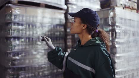 un retrato de una mujer afroamericana con un uniforme verde especial cuenta las cajas en una planta de reciclaje de residuos. fondo de la fábrica. procesamiento de materias primas, reciclaje. control de la contaminación