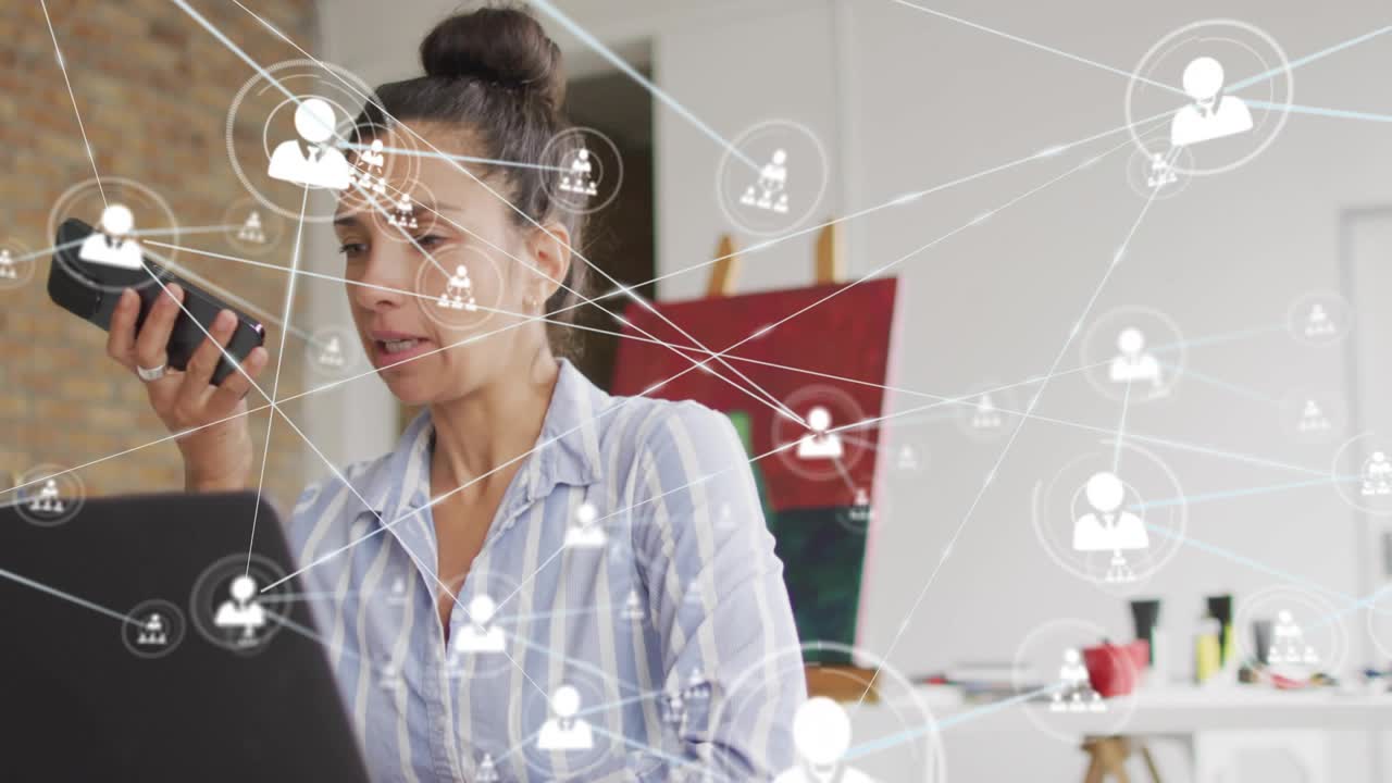 Woman talking into phone at laptop in art studio, network icons radiating across frame to connect