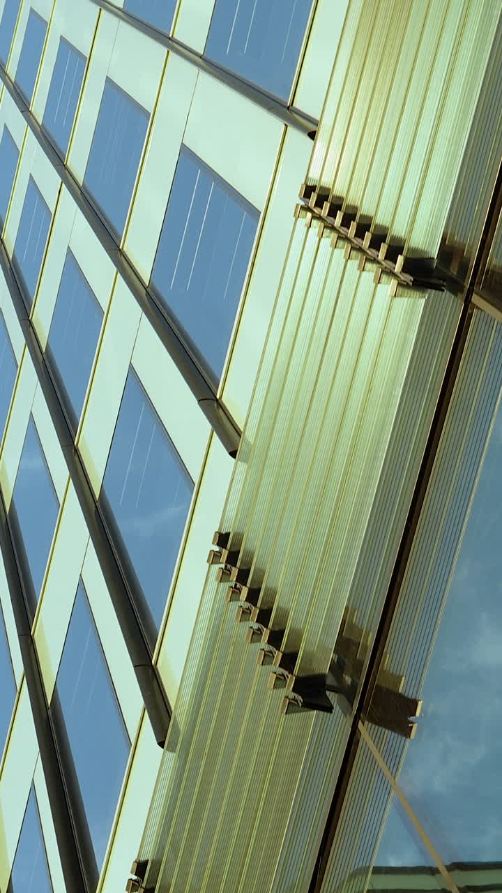 Et vertikalt lavvinkelbillede af en moderne kontorbygning i glas med gyldne refleksioner, perfekt til indhold om virksomheder og byudvikling.