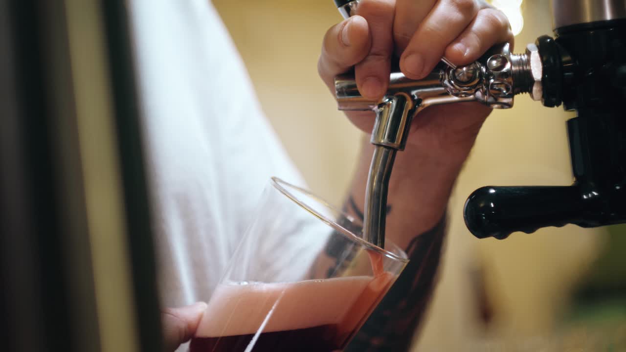 Primo piano di una mano che versa birra artigianale rossa dal rubinetto nel bicchiere