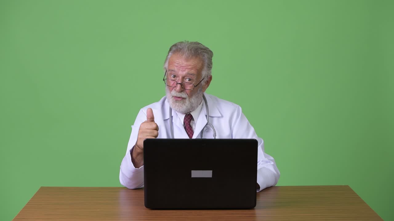 Medico anziano affascinante con la barba su sfondo verde.