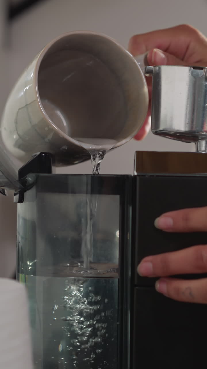 mujer llena el tanque de la máquina de café con agua de cerca. dama vierte agua de la taza en el tanque del fabricante para preparar bebida energética. mantenimiento dispositivo moderno