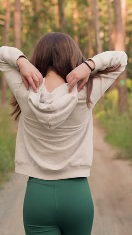 mujer se pone la capucha corriendo en el bosque. joven hace deportes corriendo a lo largo de un camino rodeado de hierba y árboles. jogging activo en la naturaleza en un día soleado de verano