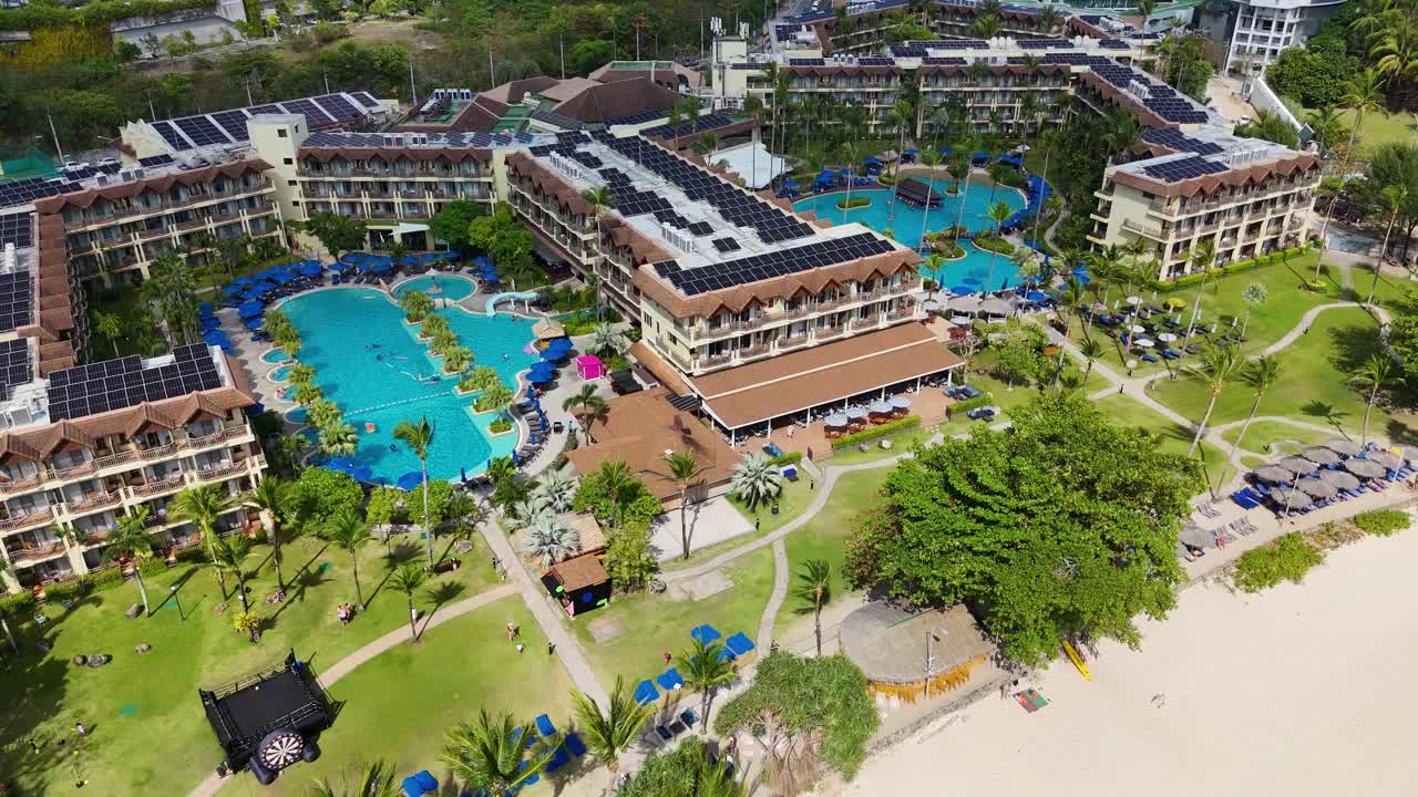 Drone footage captures a luxury resort in Phuket, showcasing pools, lush greenery, and beachfront views under bright daylight