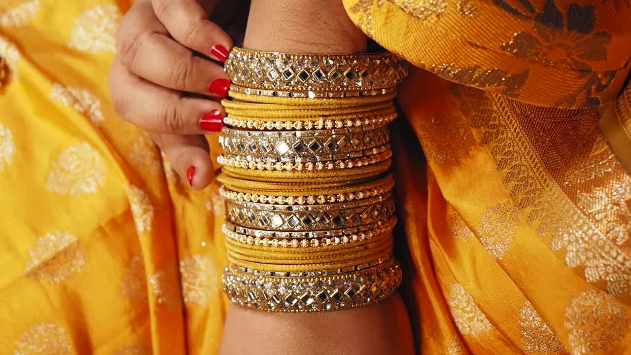 Close-up of a person's arm adorned with traditional Indian bangles and a yellow outfit