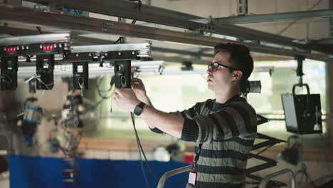 technician working on adjusting and securing lighting control unit, ensuring proper alignment in overhead production rig, preparing studio lighting system for precise use in production environment