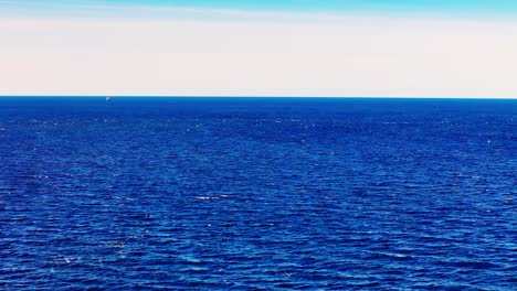a vast expanse of deep blue water stretches calmly to a soft horizon, creating a tranquil and limitless seascape under a pale open sky.