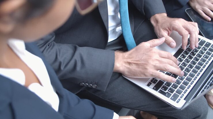 Nahaufnahme eines unerkenntlichen Geschäftsmannes, der bei Partnern oder Kollegen sitzt und auf seinem Laptop tippt