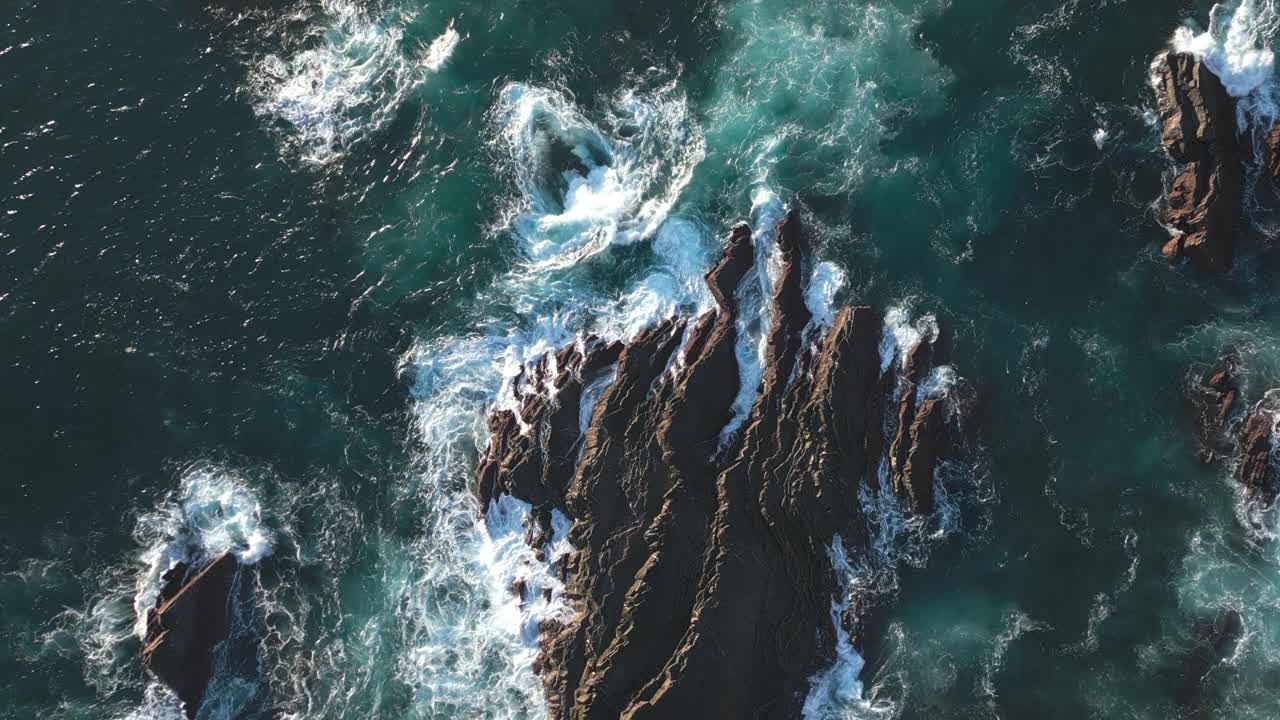 Onde oceaniche che si infrangono su scogliere rocciose, acqua di mare agitata, vista dall'alto con drone