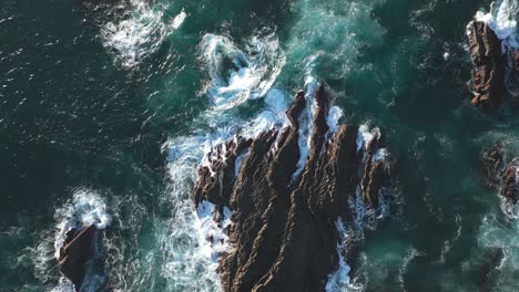 Ocean-waves-crashing-over-rocky-cliffs,-rough-sea-water,-drone-top-down-view