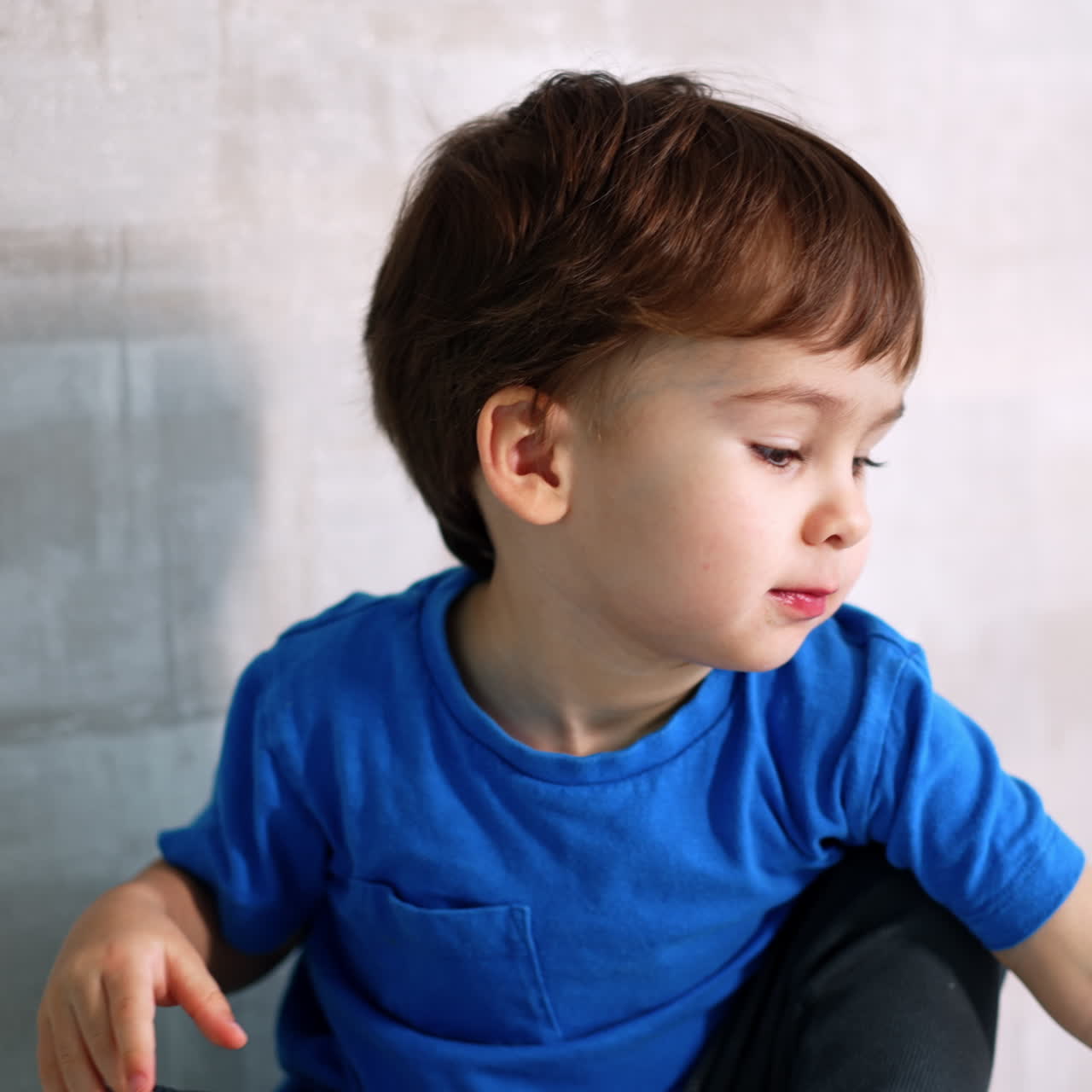 Un bambino piccolo con una maglietta blu è seduto contro il muro. Primo piano. Il bambino adorabile gioca con una mela rossa.