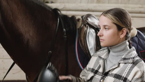 young woman putting a helmet on and petting a brown horse