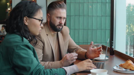 Diversos-Compañeros-De-Trabajo-Hablando-Y-Usando-Una-Computadora-Portátil-En-El-Café