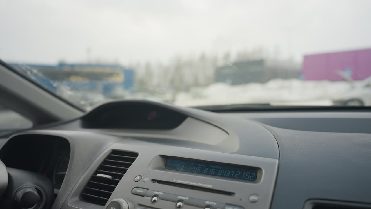 car dashboard interior showing control panel and compact disc changer with digital display screen and blurred snowy outdoor scenery visible through windshield on cold winter day