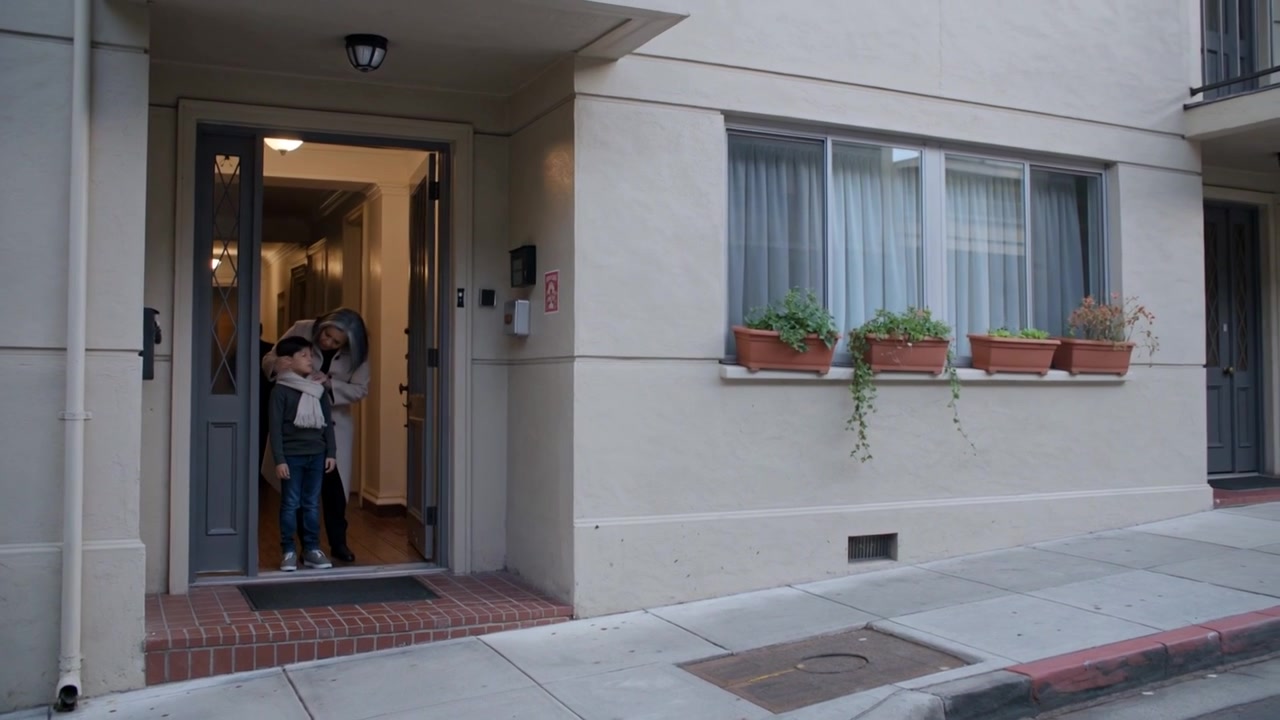 Porta a abrir-se, mulher de casaco a ajustar o cachecol do menino à entrada, a guiá-lo para o passeio, com espaço para texto