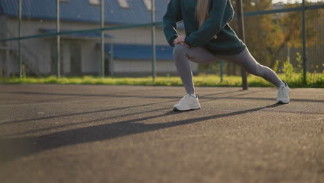 partial view of lady stretching in outdoor court with building and greenery in the background, focusing on flexibility, workout, and healthy lifestyle in an active environment