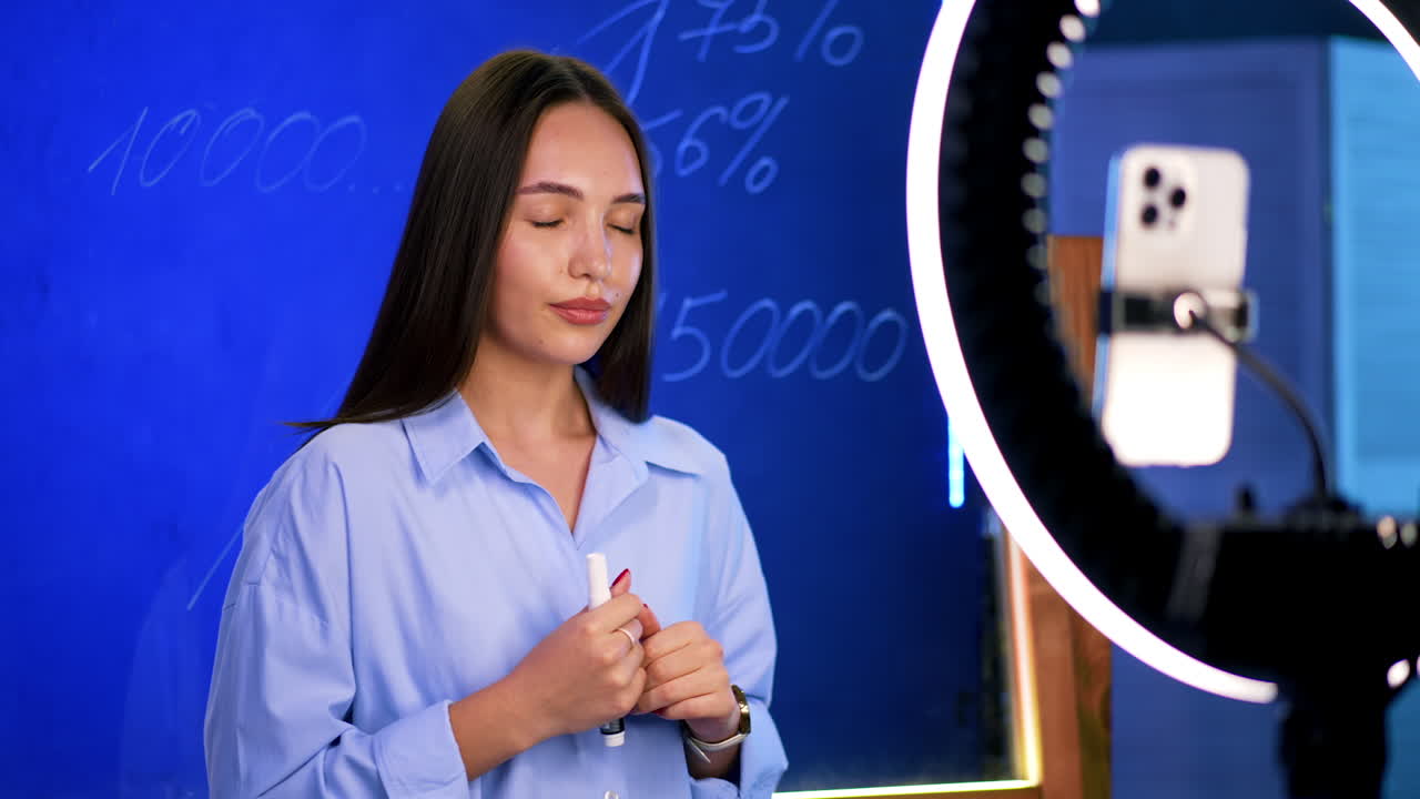 Young woman shares online lessons. A woman in a blue shirt shares knowledge while speaking in front of a recording setup and a camera
