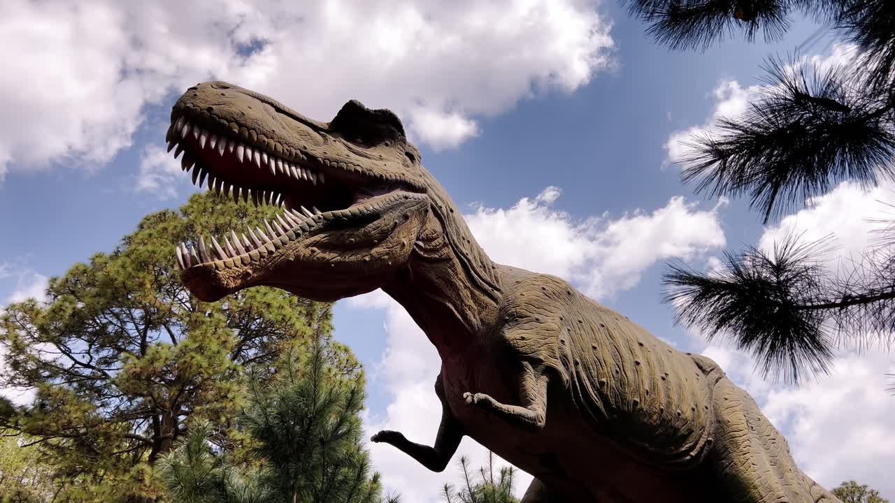 A large, realistic dinosaur sculpture standing under a blue sky with trees around
