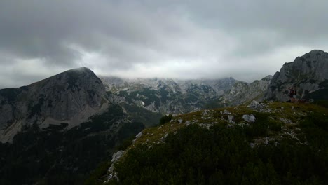 drone footage going backward over a small mountain overlooking bigger mountains in bad weather with clouds filmed in slovenian mountains in the alps