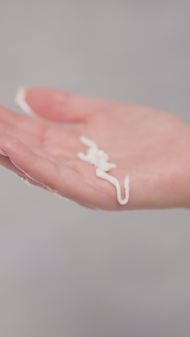 mujer vierte crema líquida para la cara en la mano en la ducha. la emulsión facial cremosa gotea sobre la mano femenina en una habitación espaciosa con fondo borroso