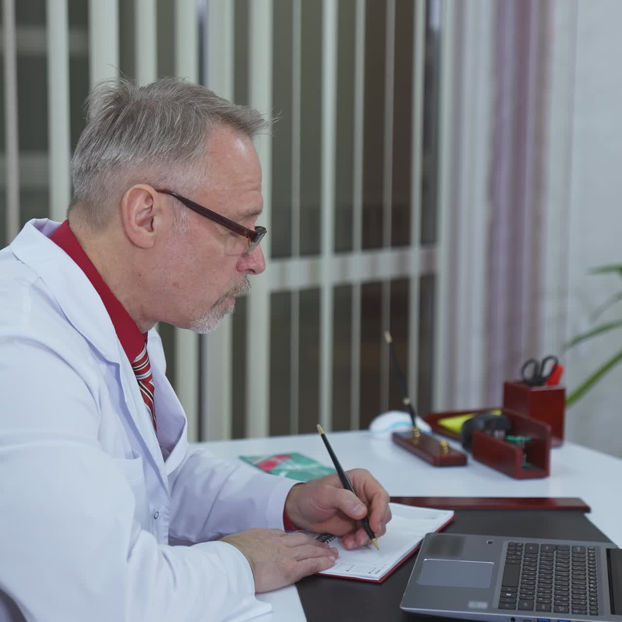 Consultazione a distanza dall'ospedale. Terapista familiare che parla con il paziente tramite laptop. Medico che parla con un paziente online e scrive nel suo taccuino.