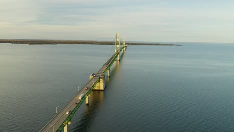 high aerial following traffic driving over long suspension bridge, calm water, wide shot