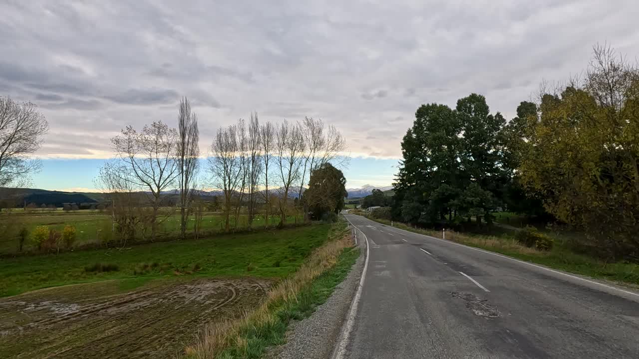 A 30-second drive along a rural highway in Akaroa, New Zealand, showcasing lush greenery and expansive skies under soft lighting