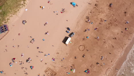 Rotación-Aérea-De-Bañistas-Relajándose-Bajo-El-Sol-En-Una-Playa-De-Arena-Dorada