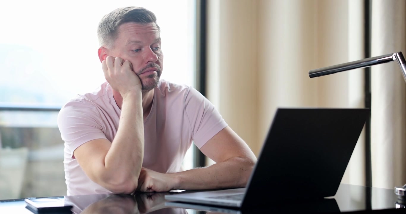 Man leans head on hand showing tired remote posture at table
