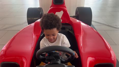 3 year-old black child driving a red f1 toy car inside a mall