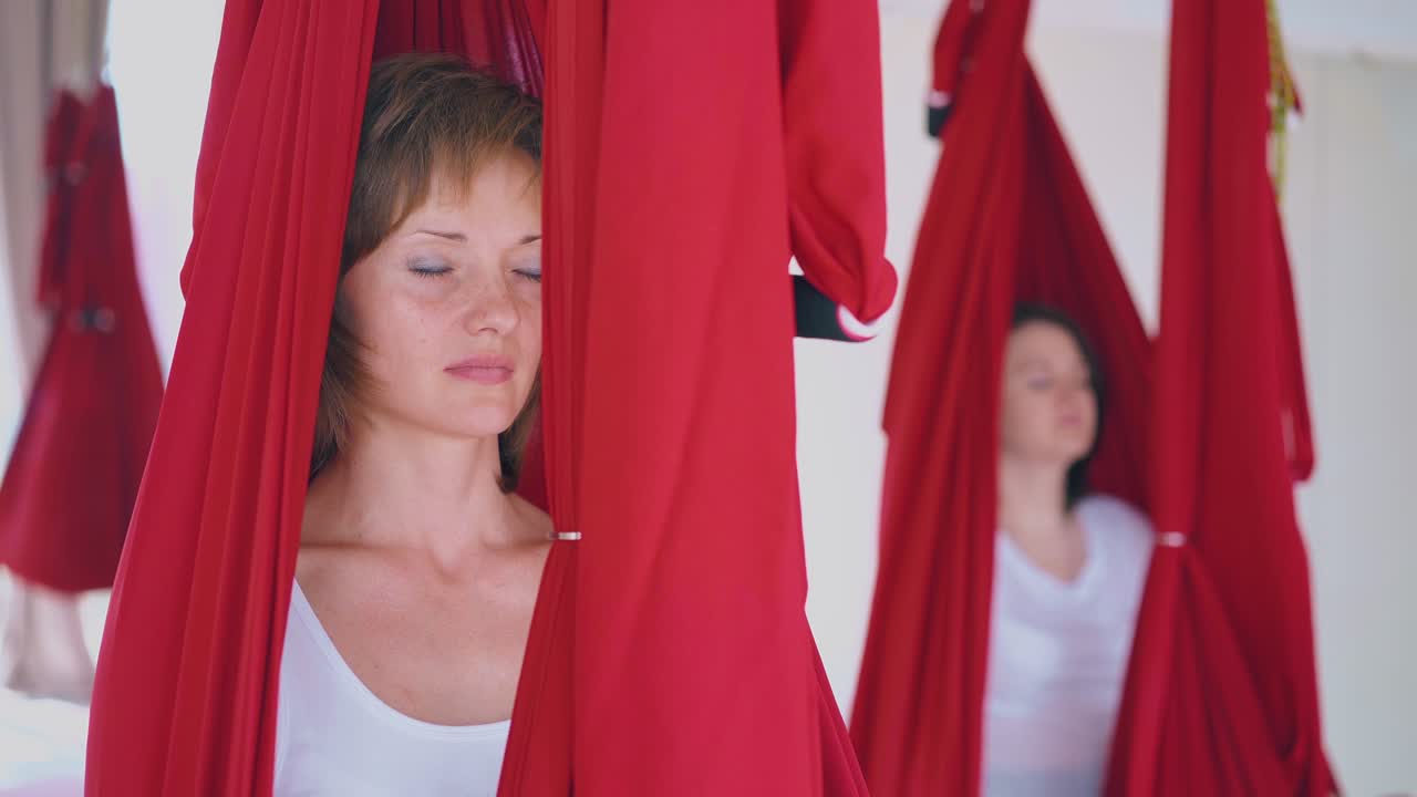 una buena mujer joven se sienta con los ojos cerrados en una hamaca de yoga de mosca