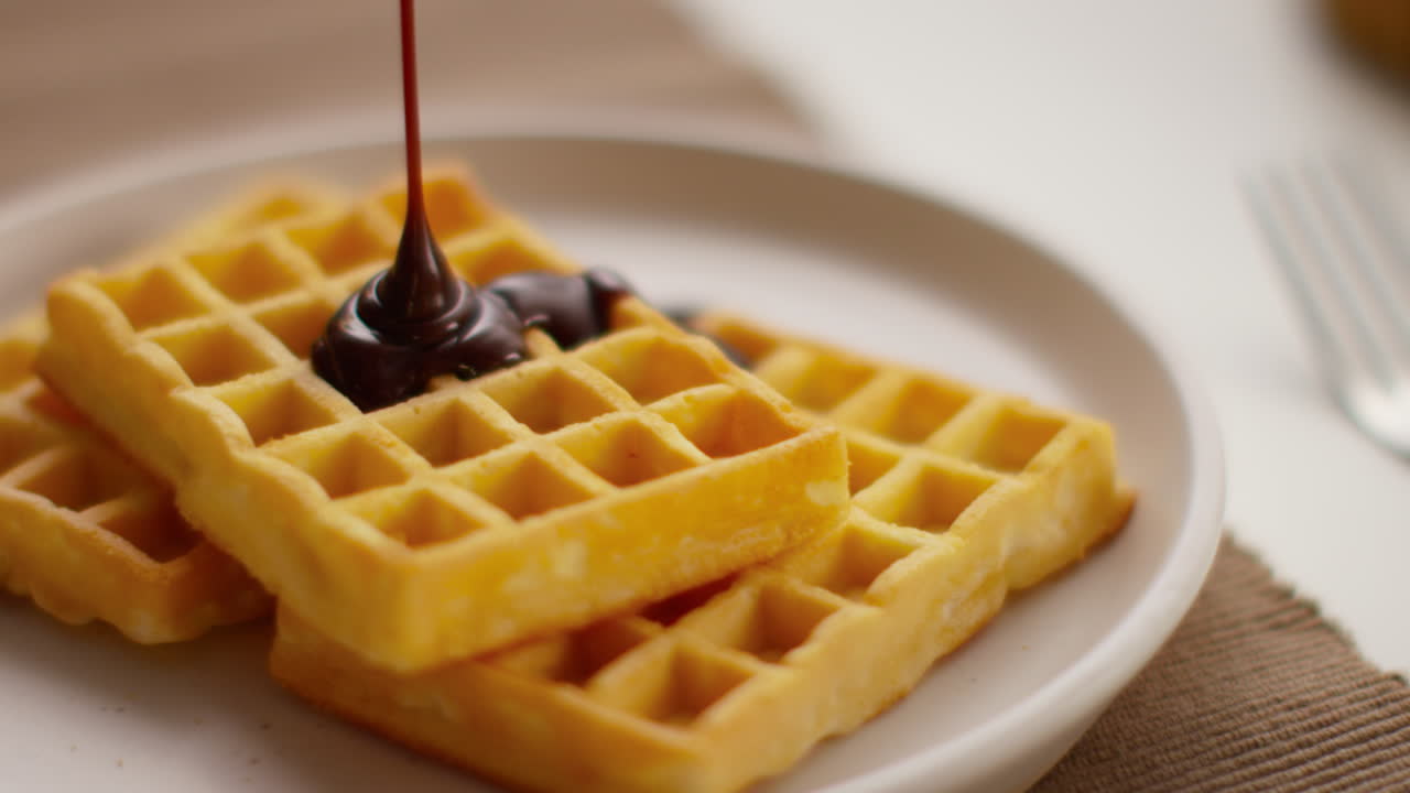 접시 1 위에 있는 와플의 어리 위에 녹은 초콜릿 소스를 부는 사람의 클로즈업