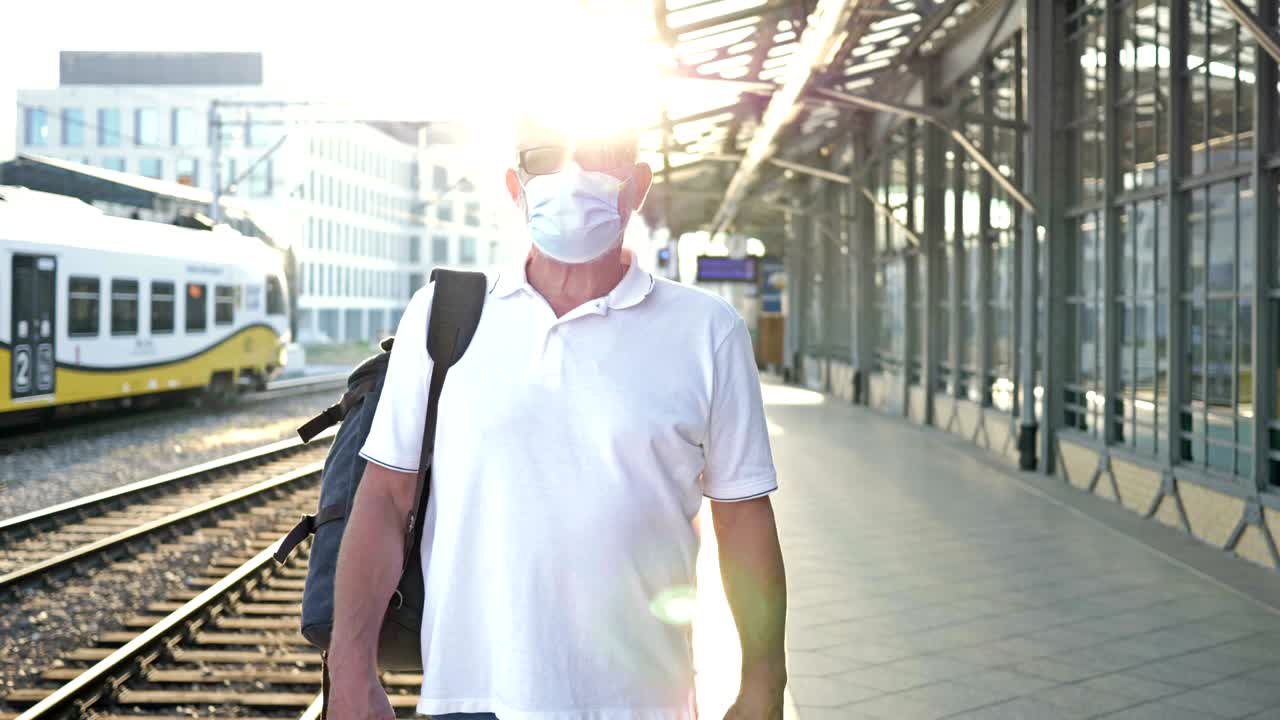 un pasajero anciano con una máscara médica en la cara. está de pie en la plataforma esperando su tren. viajes, turismo durante la epidemia de covid-19