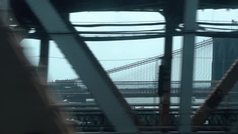 Mirando-Por-La-Ventana-De-Un-Tren-Subterráneo-De-La-Ciudad-De-Nueva-York-En-Movimiento-Pasando-Por-El-Puente-De-Manhattan-Con-El-Puente-De-Brooklyn-En-El-Fondo