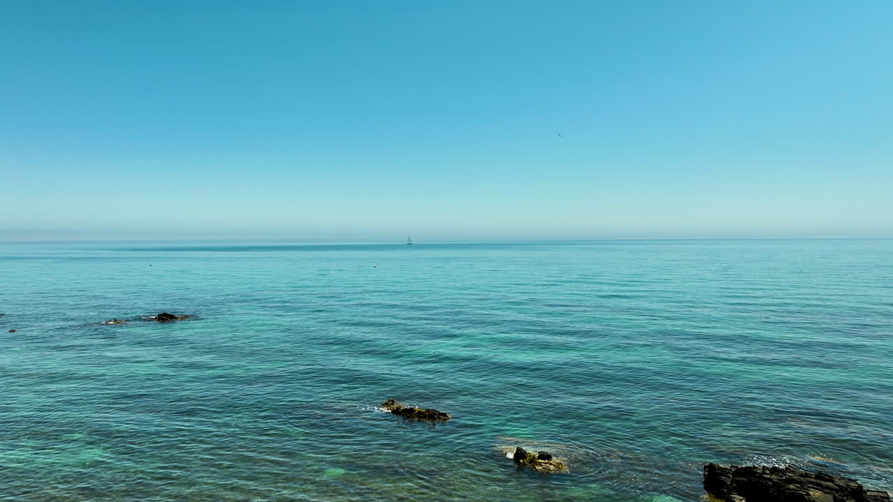 Calm sea with crystal clear turquoise water, distant horizon, and clear blue sky in Spain.