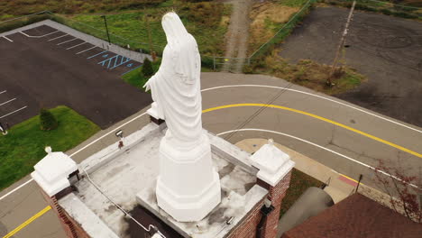 an aerial view of a statue of the virgin mary on top of a catholic church in upstate, ny