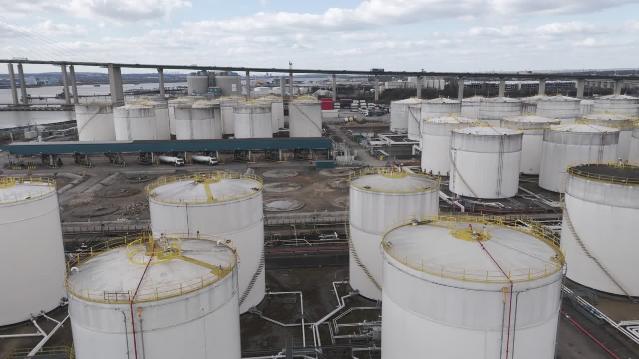 Aerial perspective of riverside cluster of domed fuel storage tanks interconnected by pipeline network and maintenance roads, representing critical downstream energy infrastructure