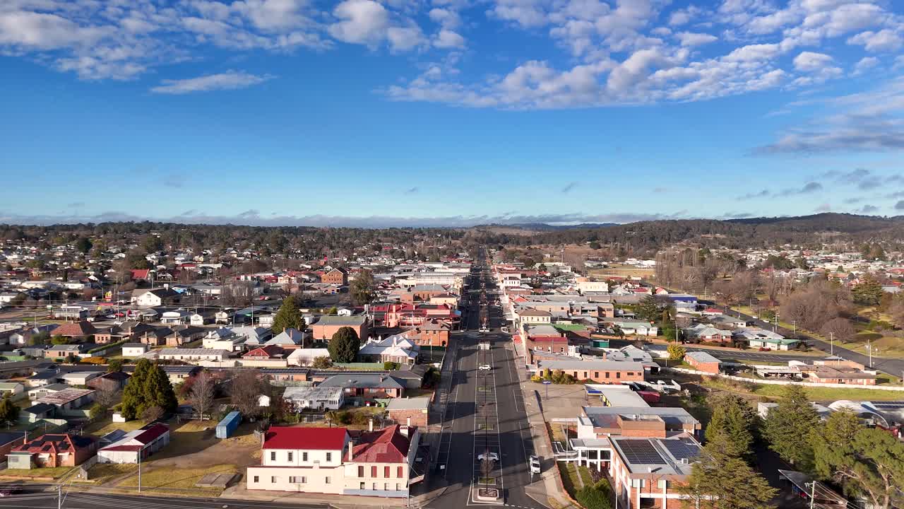 Aerial drone footage glides above a quiet main street in a small Australian town, showing residential and commercial buildings under bright, clear daylight