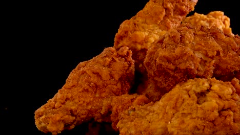 crispy, golden fried chicken wings and breasts rotate and zoom in slow motion against a black background, highlighting texture and spicy seasoning under dramatic lighting