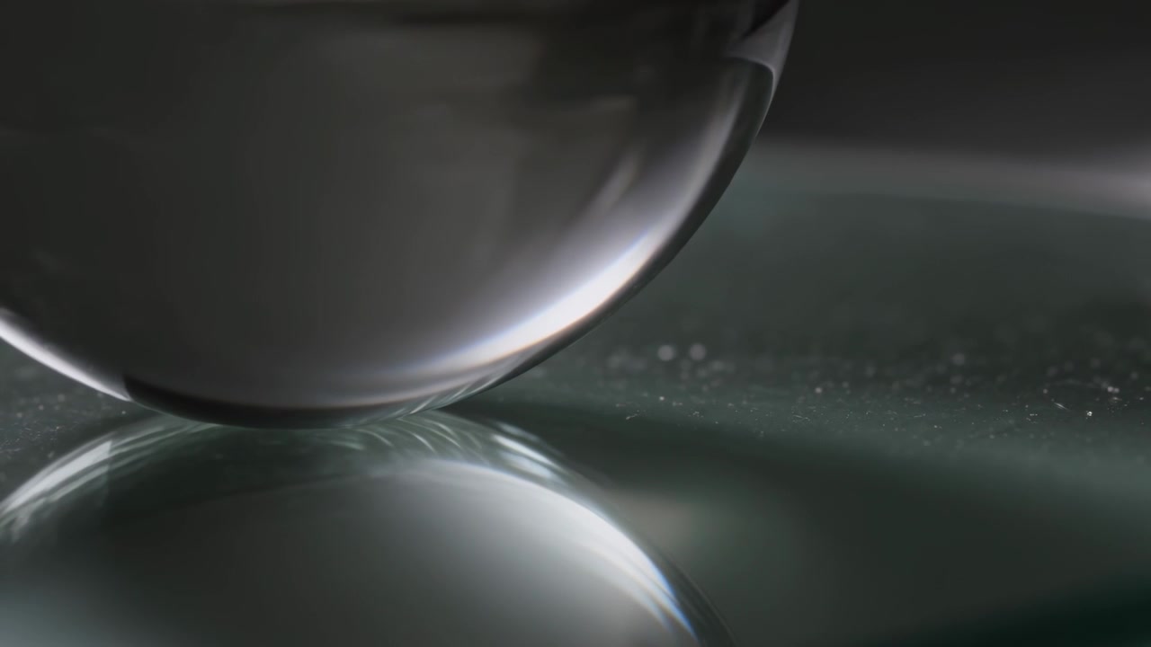 Starting motion, large glass orb descending to glossy panel in lab, showing highlights and specks