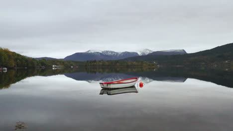 wooden rowing boat floating on calm lake with mirror reflection in norway