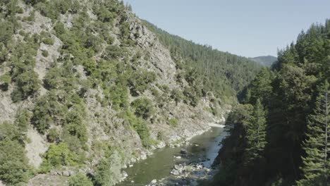 drone flies and turns corner over a rocky river surrounded by lush forest