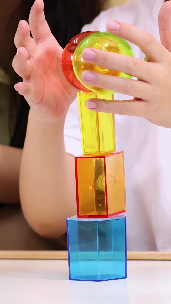 Hands Stacking Colorful Translucent Geometric Shapes