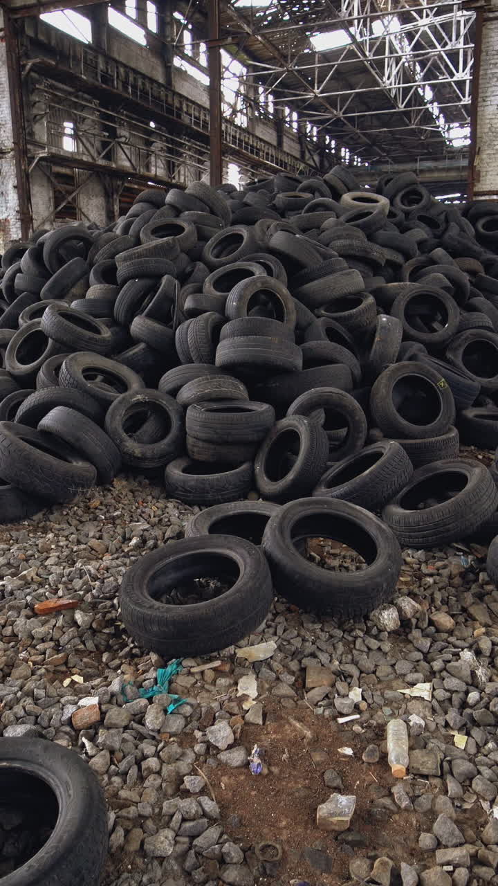 A bunch of car tires are in an abandoned high hangar with holes in the windows of building. View of old factory inside. Close-up. Vertical video