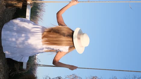a woman in a white dress and hat is relaxing in the garden and riding on a swing at sunset a woman in a white dress and hat is relaxing in the garden and riding on a swing at sunset