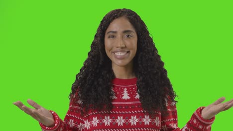 studio portrait of woman wearing christmas jumper against green screen smiling at camera saying merry christmas 2