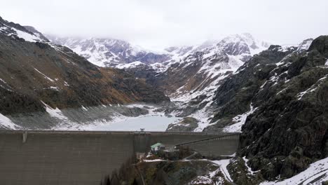 aerial view of imposing diga di gera, a hydroelectric dam, nestled amidst snow-dusted mountains in valmalenco, italian alps. engineering and renewable energy. aerial backward, copy space
